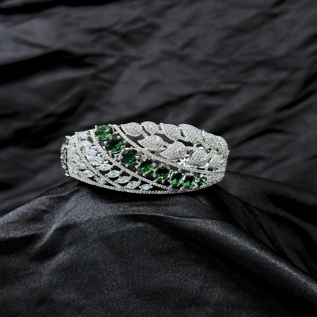Silver bracelet with AD leaf design and green gemstones on a black fabric background