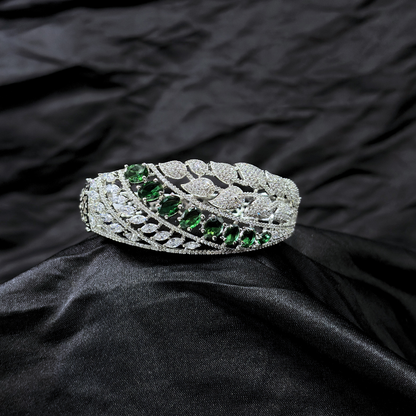 Silver bracelet with AD leaf design and green gemstones on a black fabric background