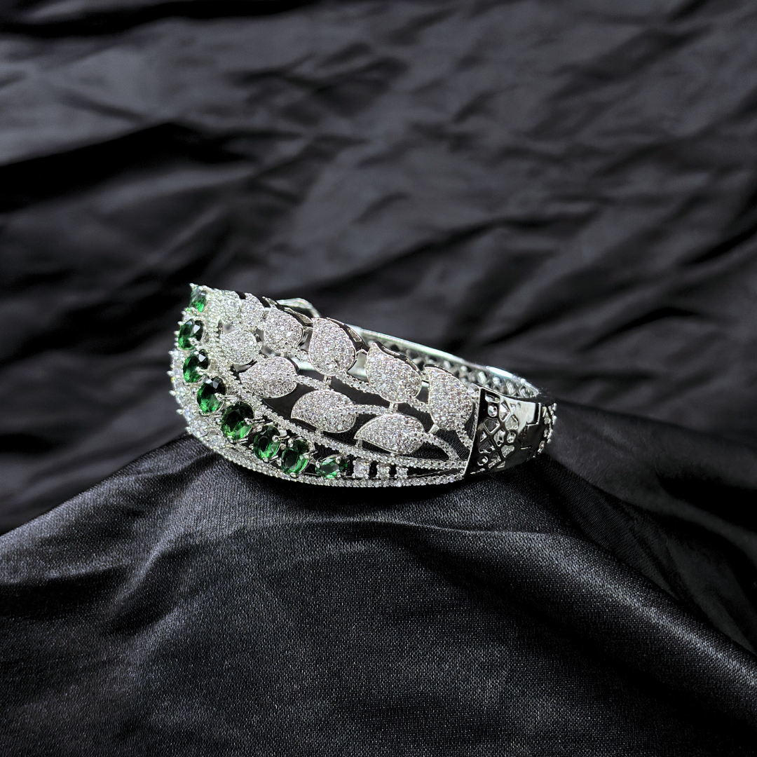 Silver bracelet with AD leaf design and green gemstones on a black fabric background