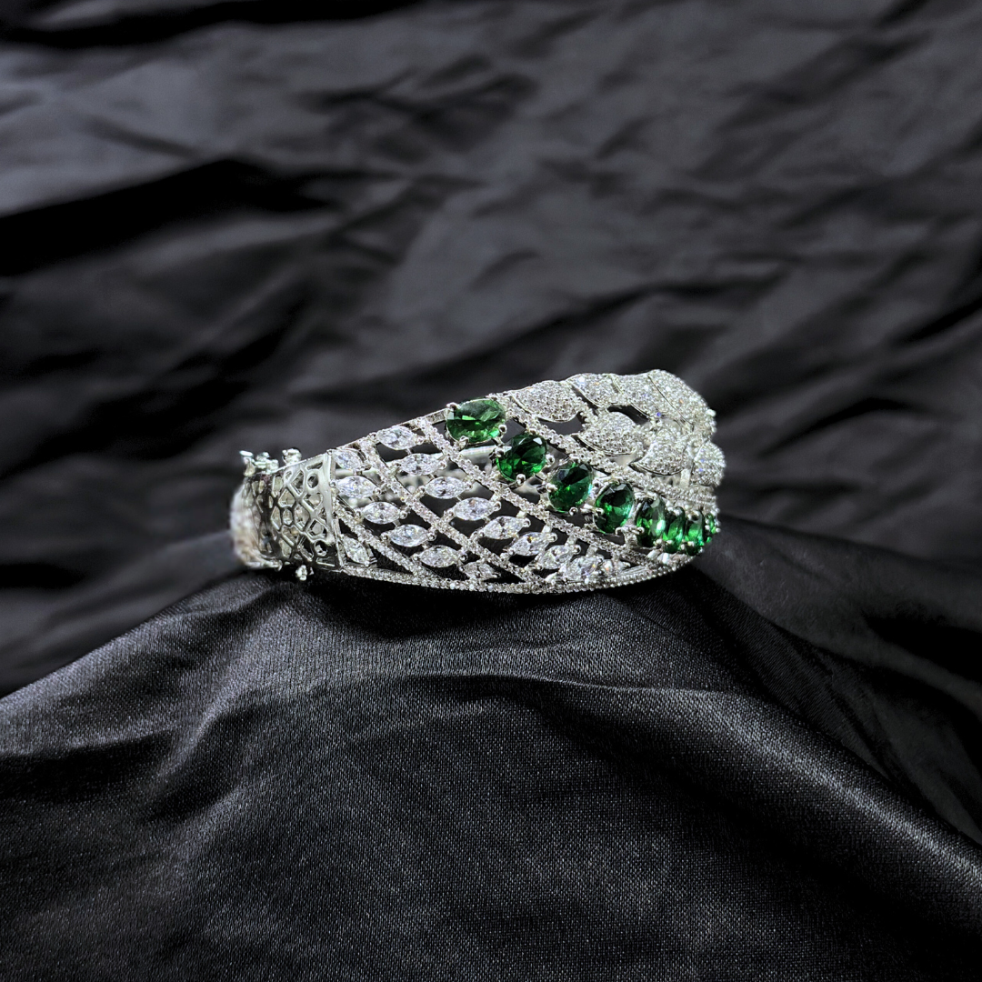 Silver bracelet with AD leaf design and green gemstones on a black fabric background
