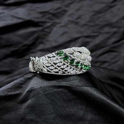 Silver bracelet with AD leaf design and green gemstones on a black fabric background