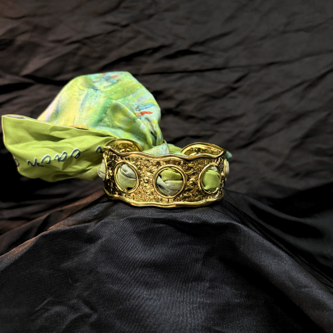 Gold textured bracelet with a green decorative silk scarf on a black fabric background