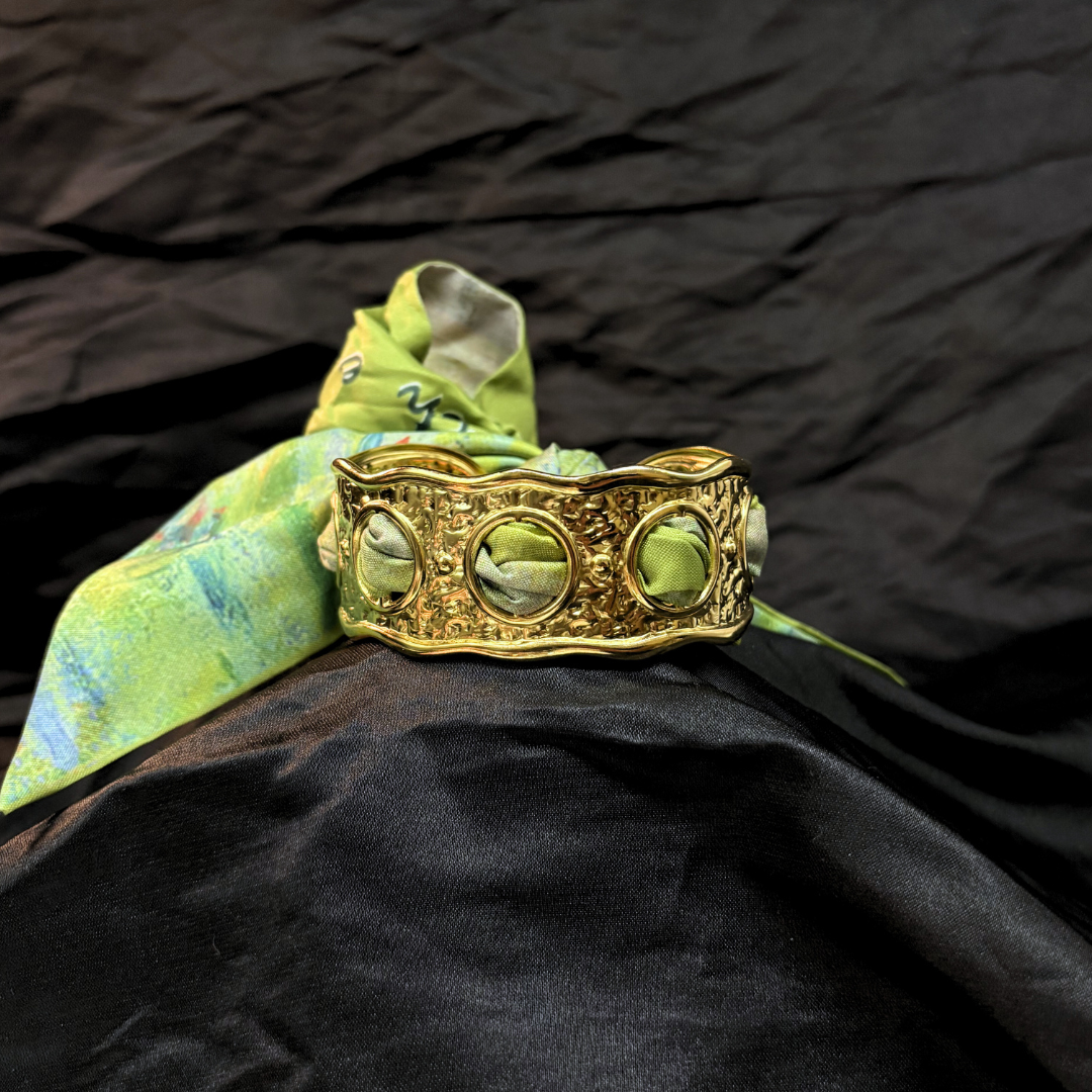 Gold textured bracelet with a green decorative silk scarf on a black fabric background