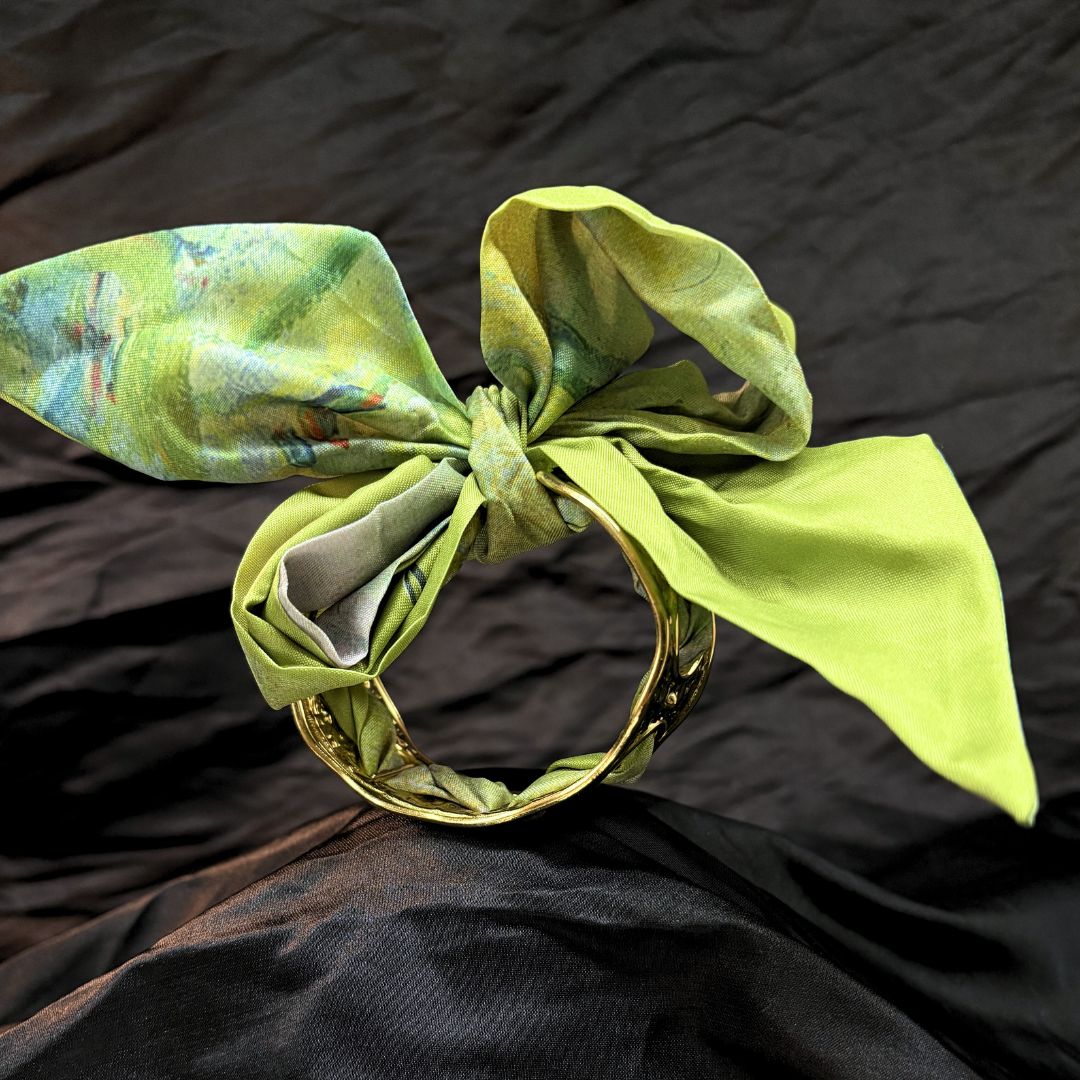 Gold textured bracelet with a green decorative silk scarf on a black fabric background