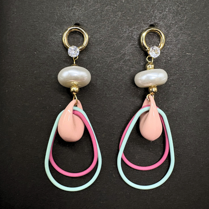 Pair of earrings with pink and mint teardrop wire shapes inside a peach ceramic hoops, a pearl donut and AD stones on a dark background