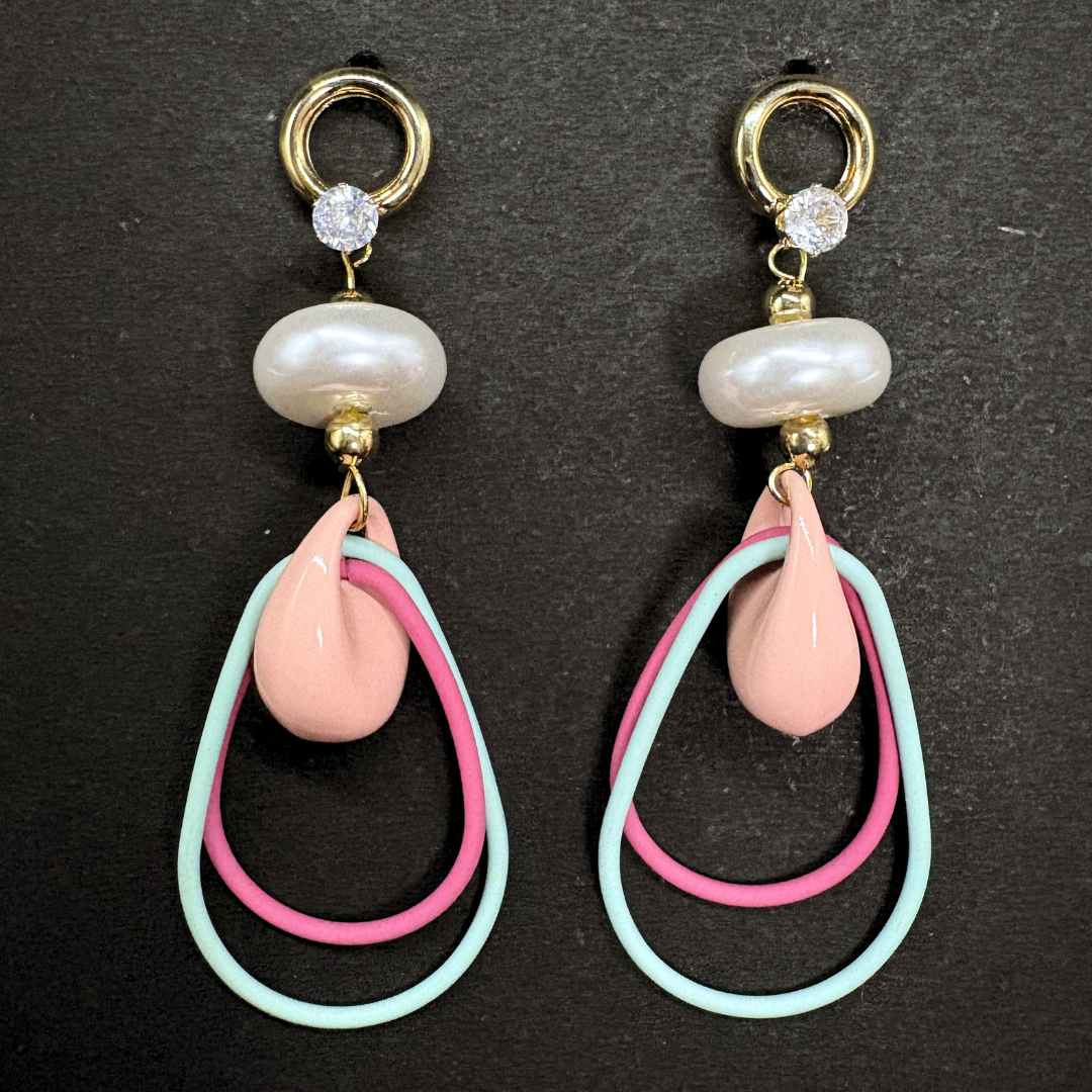 Pair of earrings with pink and mint teardrop wire shapes inside a peach ceramic hoops, a pearl donut and AD stones on a dark background