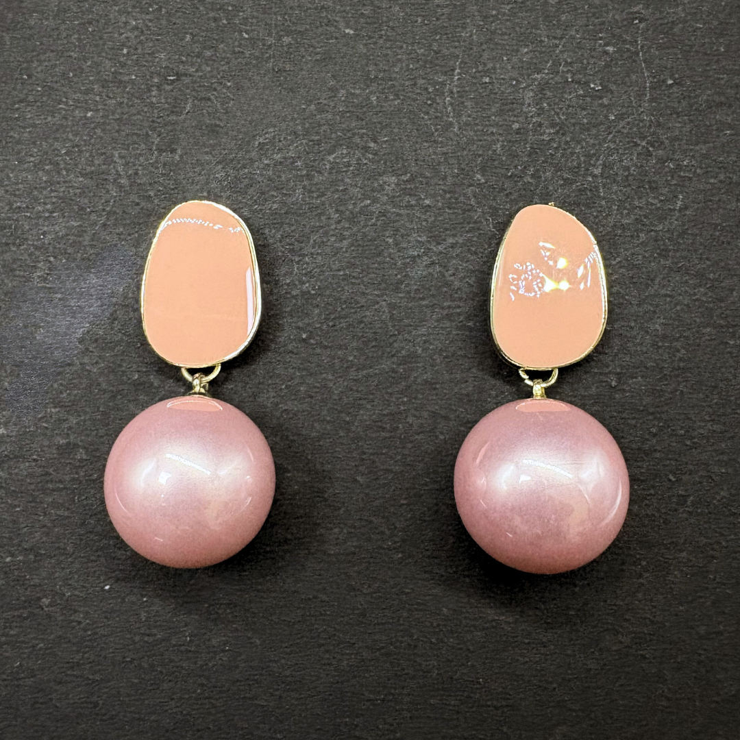 Pair of earrings with pink pearls and peach-colored oval enamel on a dark background