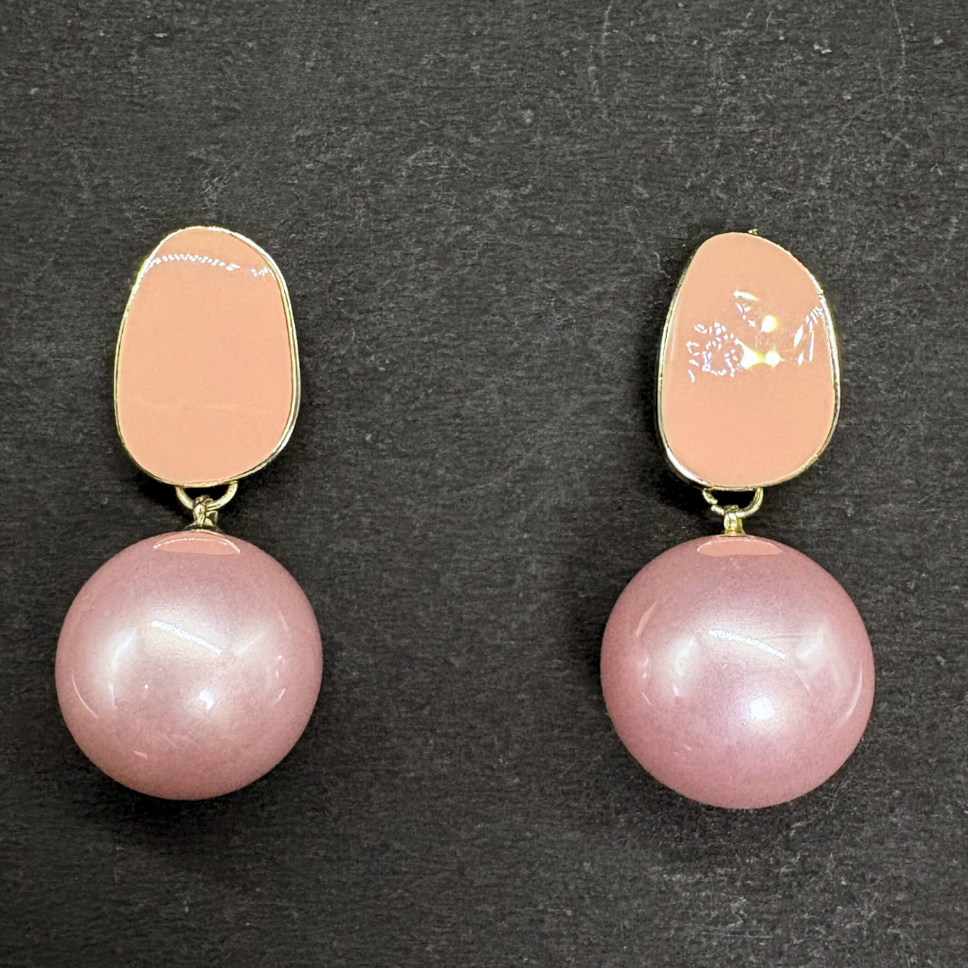 Pair of earrings with pink pearls and peach-colored oval enamel on a dark background