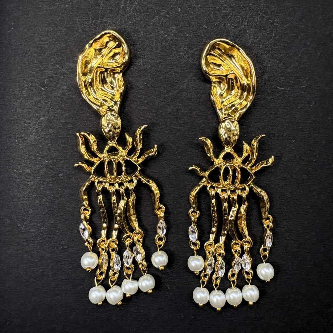 Gold and pearl schiaparelli inspired earrings on a black background
