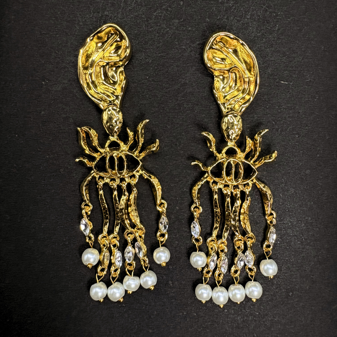 Gold and pearl schiaparelli inspired earrings on a black background