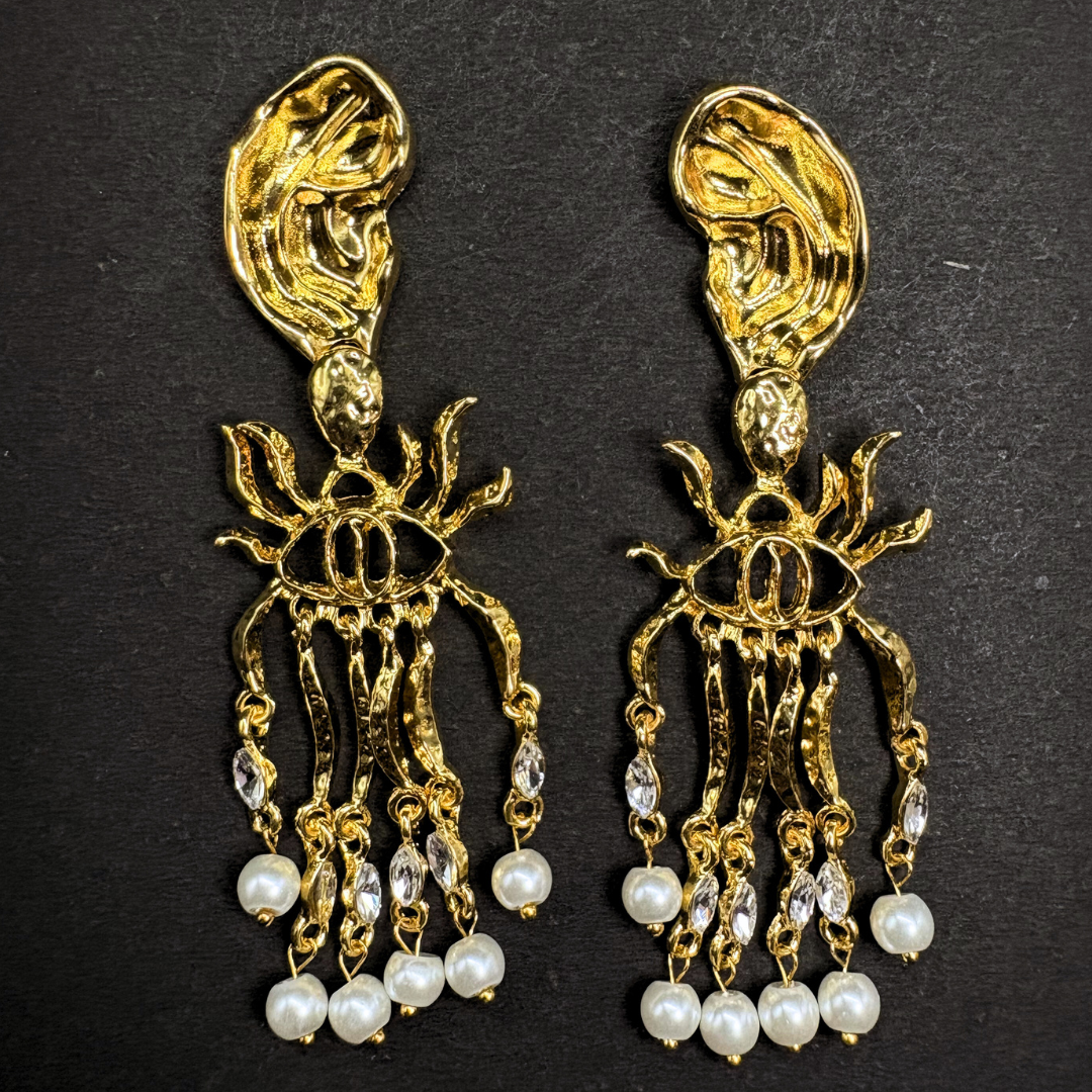 Gold and pearl schiaparelli inspired earrings on a black background
