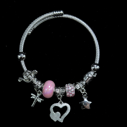 Bracelet with various charms including a pink bead, hearts, music notes, dragon fly  and star on a black background