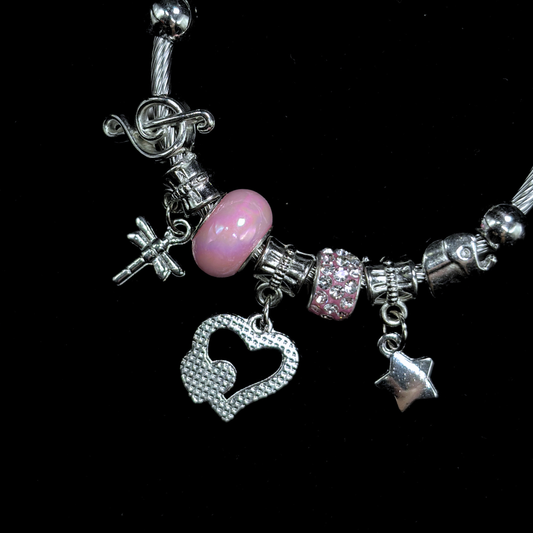 Bracelet with various charms including a pink bead, hearts, music notes, dragon fly  and star on a black background