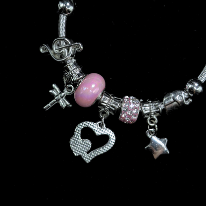 Bracelet with various charms including a pink bead, hearts, music notes, dragon fly  and star on a black background