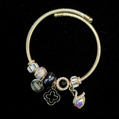 Charm Bracelet with various charms of an AD and iridescent stone swan, black bead, LV clover  on a black background
